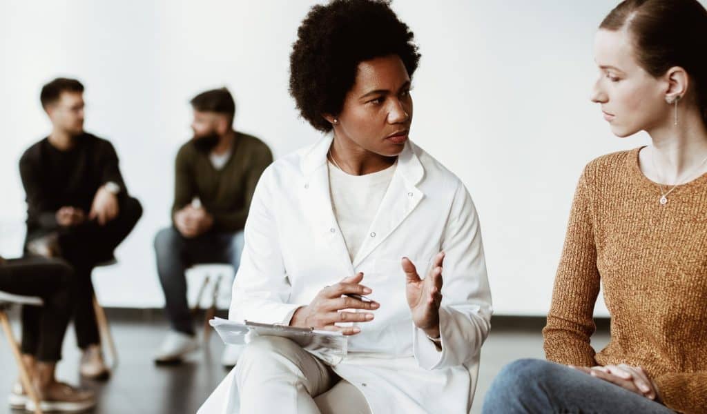 African American psychotherapist and young woman communicating while having group meeting.